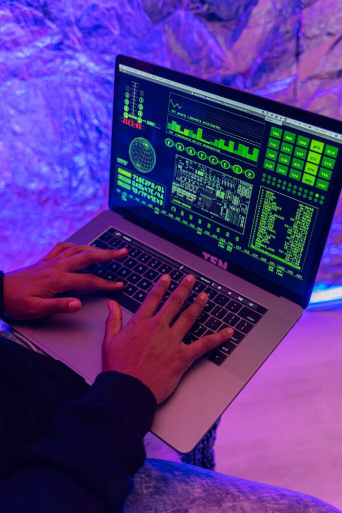 Close-up of hands typing on a laptop displaying green code, indoors, purple lighting.